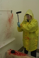 Person in rain gear hitting blood so it splatters on wall to demonstrate blood splatter during a crime scene